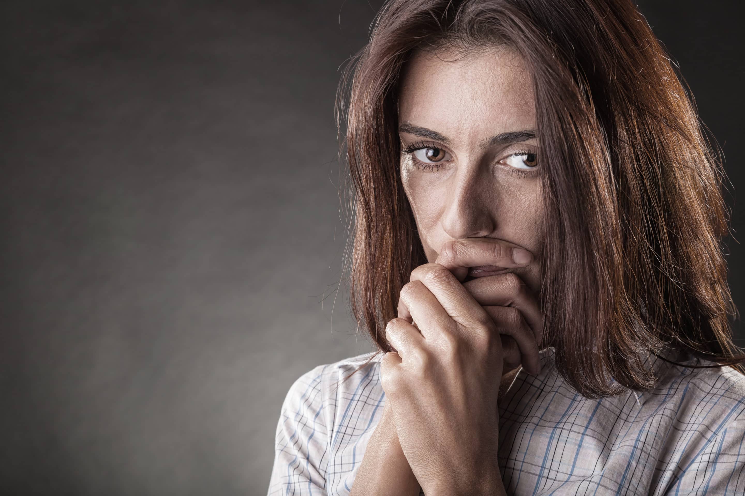 Femme le regard inquiet, les mains jointes devant la bouche, évoquant la vulnérabilité et le courage d’un témoignage intime.